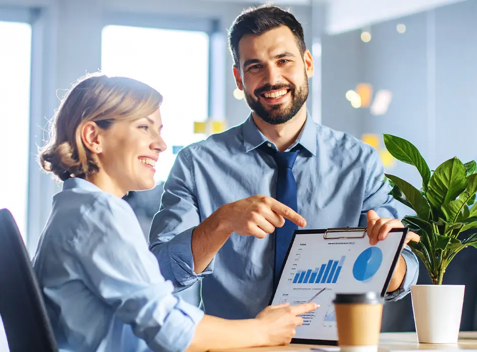 Deux employés souriant de la firme de comptable LGMC qui pointe des résultats sur un tableau électronique.